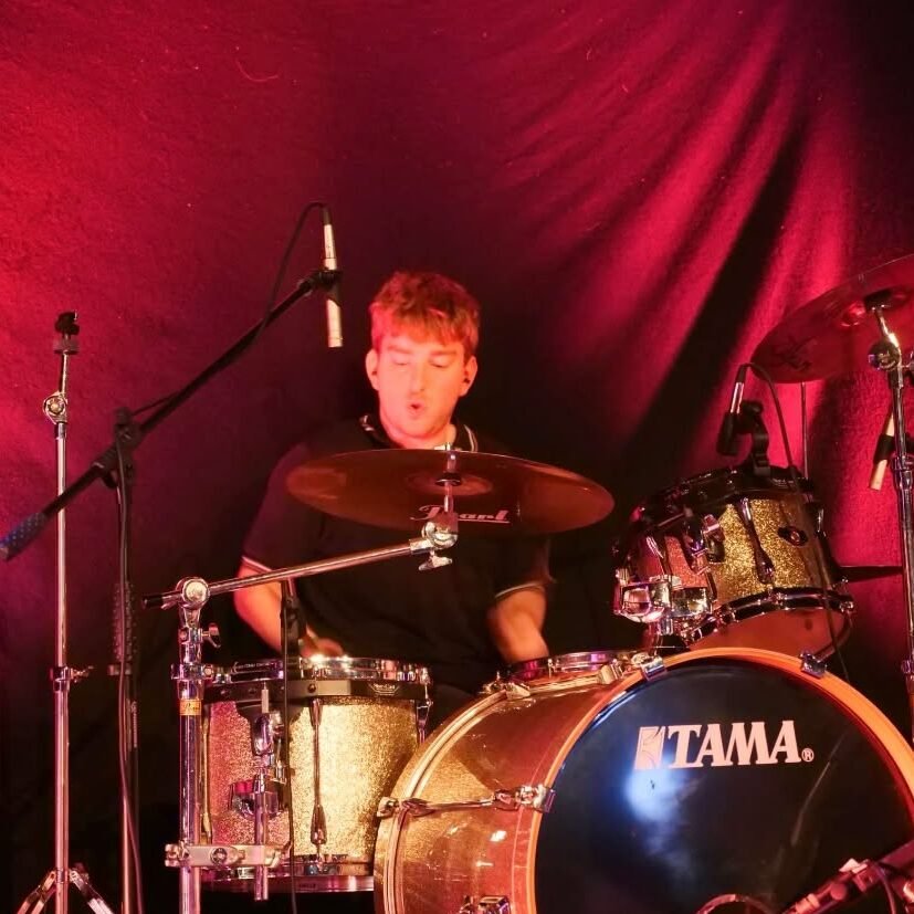 Jensen drumming against a curtain lit with red light